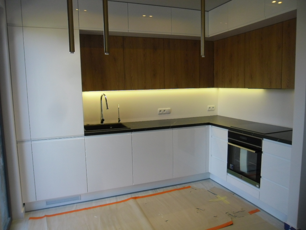 Duża kuchnia w apartamencie - białe fronty z drewnianymi górami